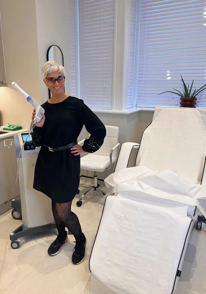 Female clinician with short gray hair and glasses holding a wand-shaped dental device in a bright clinic.